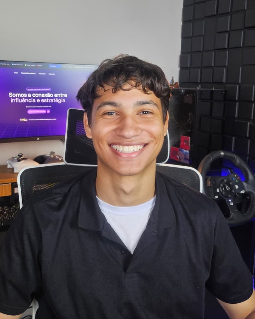 Enzo Vieira sorrindo, de camisa preta, numa estação de trabalho